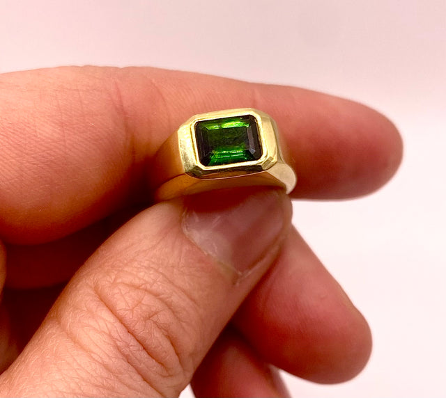 Close-up van een Beausi-ring met groene steen, vastgehouden tussen vingers